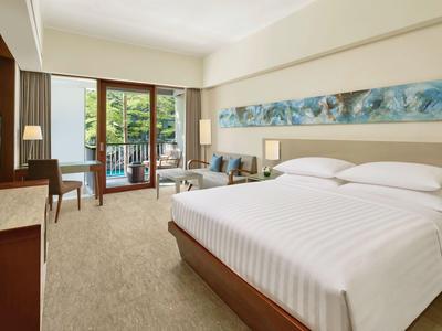 Camera d'hotel moderna con letto grande, divano e balcone con vista sulla piscina.