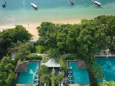Hotel mit zwei Pools und Blick auf Strand und Meer mit Booten und Bäumen dazwischen.