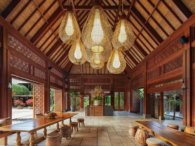 Ein offener, hölzerner Pavillon mit hohen Decken und dekorativen Lampen, umgeben von Natur.