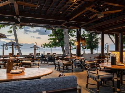 Offenes Restaurant mit Holzmöbeln und Blick auf den See bei Sonnenuntergang.