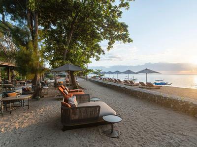 Strandhotel mit Sonnenliegen, Sonnenschirmen und Blick auf ruhiges Meer bei Sonnenuntergang.