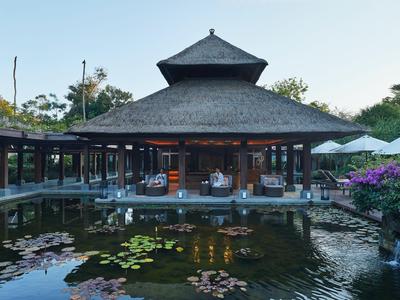 Ein Pavillon mit spitzem Dach über einem Teich mit Seerosen bei klarem Himmel.