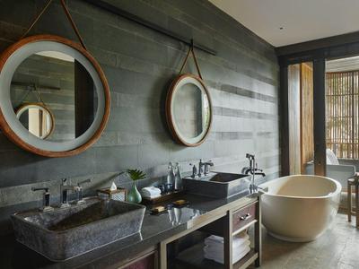 Modernes Badezimmer mit Doppelwaschbecken, runden Spiegeln, freistehender Badewanne und großem Fenster.