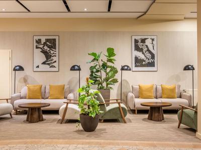 Moderner Hotel-Loungebereich mit bequemen Sofas, Holztafeln und grünen Pflanzen.