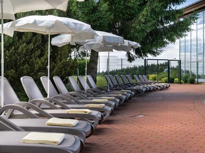 Reihe von Liegestühlen mit weißen Handtüchern und Sonnenschirmen neben einem Pool.