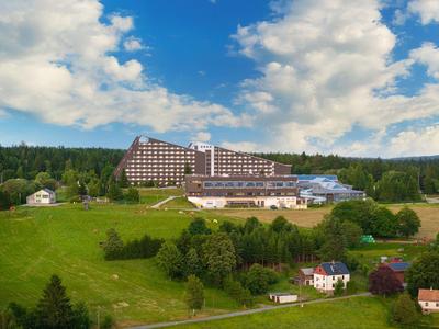 Großes Hotelgebäude auf grünem Hügel unter bewölktem blauem Himmel.