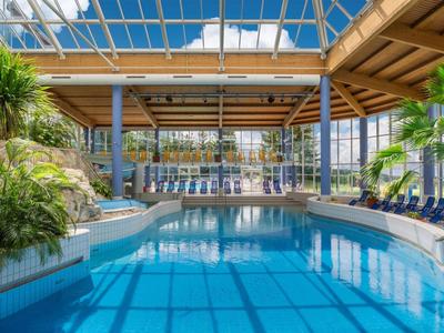 Überdachter Poolbereich mit blauen Liegestühlen und tropischen Pflanzen in einem Hotel.