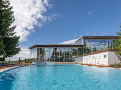 Ein großer Außenpool vor einem modernen Hotelgebäude mit Glasfassade und umgeben von Bäumen.