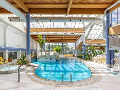 Helles Hallenbad mit Pool, modernen Möbeln und Pflanzen in einem Hotel.