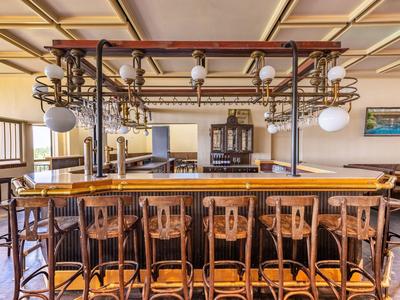 Traditionelle Bar mit hölzernen Stühlen und Vintage-Beleuchtung in hellem, gemütlichem Raum.