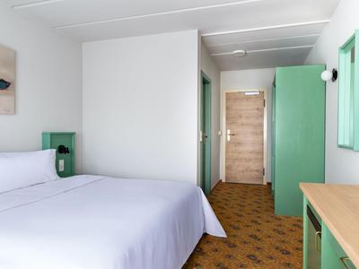Modernes Hotelzimmer mit großem Bett, grünem Schrank, Holztür und Holzboden.