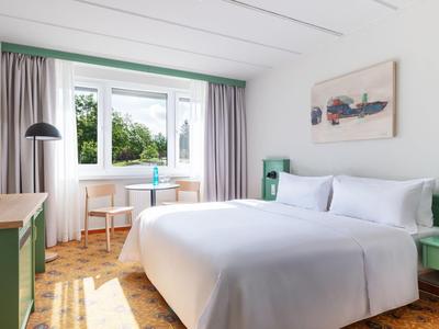 Helles Hotelzimmer mit großem Fenster, Doppelbett, grün gestrichenen Möbeln und Holzboden.
