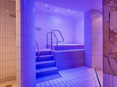 Moderner Wellnessbereich mit Treppe, Whirlpool und heller Fliesenwand in lila Licht.