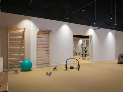 Moderner Fitnessraum mit hellen Wänden, Holzstangen und verschiedenen Trainingsgeräten.