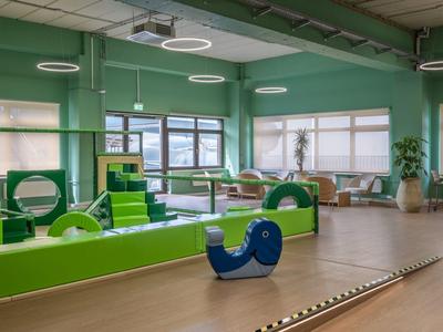 Heller, grüner Kinderspielraum mit verschiedenen Spielgeräten und großen Fenstern.