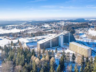 Hotelkomplex mit mehreren Gebäuden umgeben von schneebedeckten Wäldern und Bergen unter blauem Himmel.