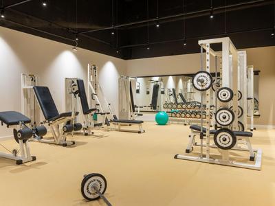 Moderner Fitnessraum mit verschiedenen Trainingsgeräten und Hanteln in einem Hotel.