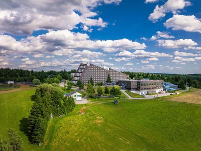 Modernes Hotelgebäude mit Wiese und bewaldetem Hintergrund unter blauem Himmel mit Wolken.