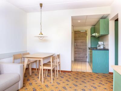 Heller Essbereich mit Holztisch und Stühlen neben einer kleinen grünen Küchenzeile in einem Hotelzimmer.