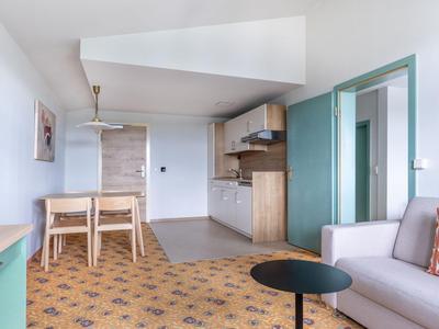 Moderner Hotelzimmerbereich mit Küchenzeile, Esstisch und gemütlichem Sofa.