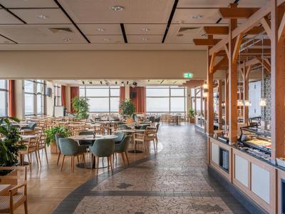 Großer, heller Speisesaal mit Tischen, Stühlen und Blick auf das Meer.