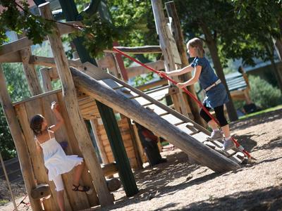 Kinder spielen auf einem hölzernen Klettergerüst mit Rutsche im sonnigen Garten.