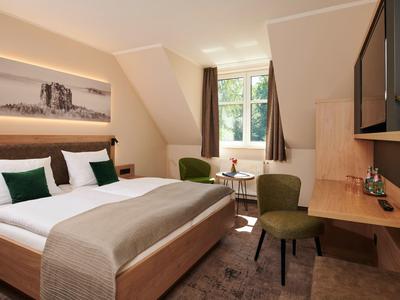 Accogliente camera d'hotel con letto matrimoniale, scrivania, sedie e finestra con tende.