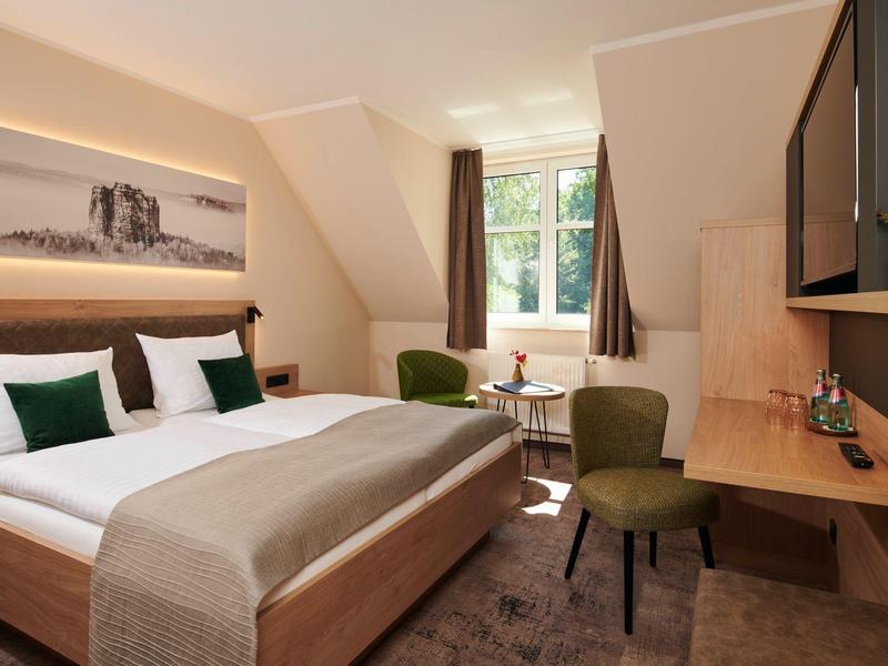 Gezellige hotelkamer met tweepersoonsbed, bureau, stoelen en raam met gordijnen.