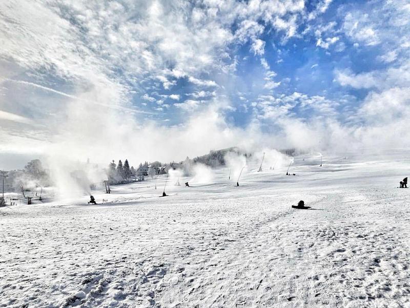 Paesaggio invernale con pendio innevato, persone che slittano e nebbia nella luce limpida del mattino
