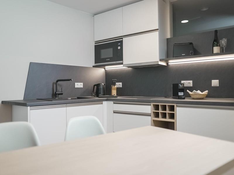 Cucina bianca moderna con piano di lavoro nero e elettrodomestici integrati in una camera d'hotel.