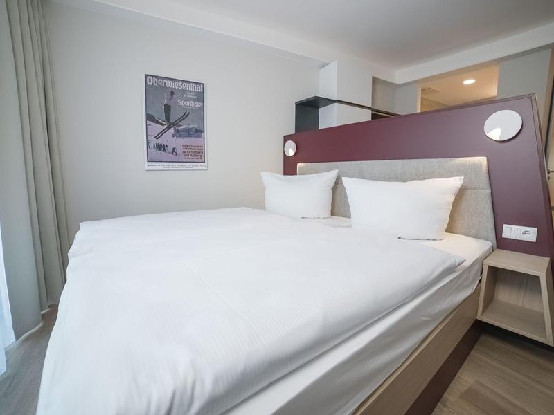 Camera d'hotel moderna con letto grande, biancheria bianca e testiera decorativa.