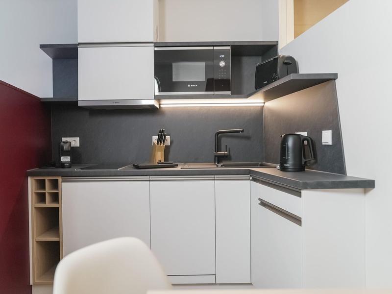 Angolo cottura moderno con piani grigi, armadietti bianchi, microonde e bollitore.