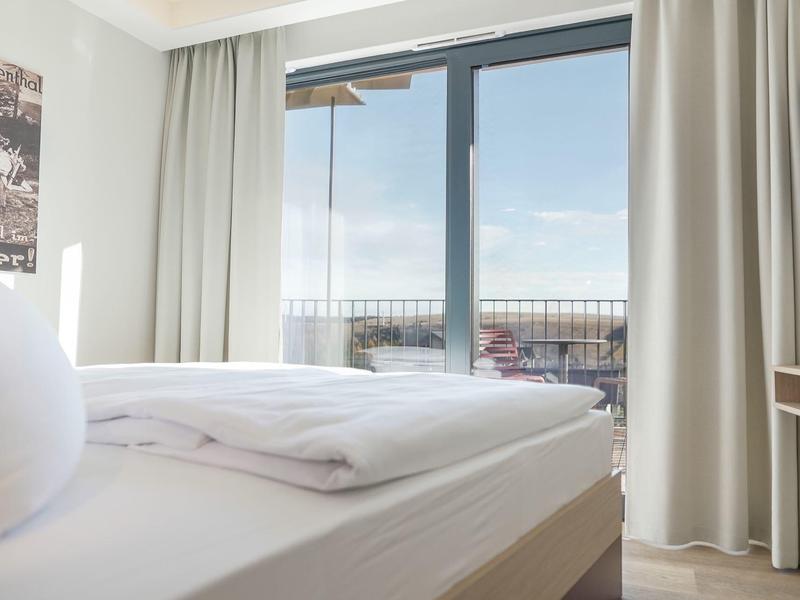 Camera d'albergo luminosa con letto accogliente e balcone con vista sul mare.