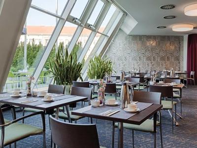 Moderner Speisesaal mit großen Fenstern, braunen Stühlen und eingedeckten Tischen, Pflanzen am Fenster.