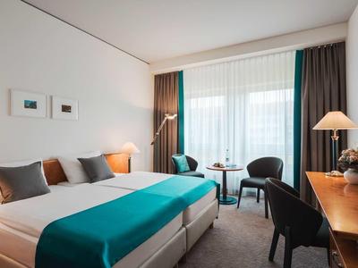 Modernes Hotelzimmer mit großem Bett, Holzschreibtisch, zwei Sesseln und bodentiefen Fenstern.