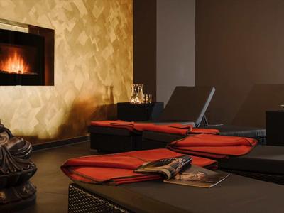 Gemütlicher Raum mit Buddha-Statue, Kamin, Liegen und roten Kissen in warmem Licht.