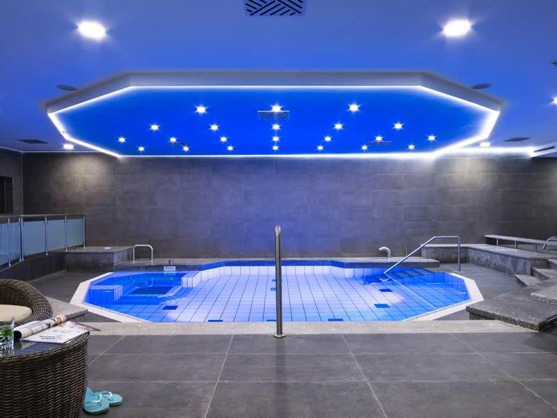 Moderner Innenpool mit blauer Beleuchtung, weißen Liegestühlen und grauen Wänden.