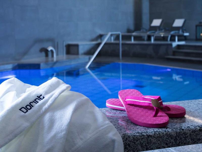 Schwimmbad mit blauem Wasser, rosa Flipflops und weißem Bademantel auf grauem Beckenrand.