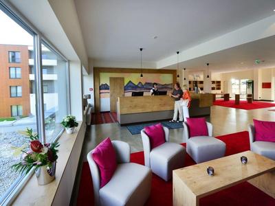 Moderne Lounge mit grauen Sesseln, pinken Kissen, Holztischen und großen Fenstern.