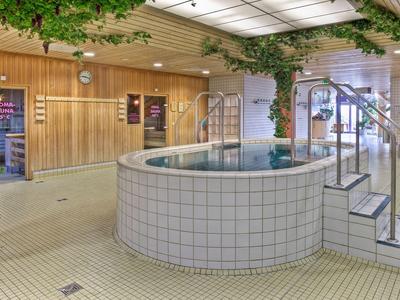 Innenansicht eines Wellnessbereichs mit rundem Whirlpool, Holzverkleidung und Pflanzen.