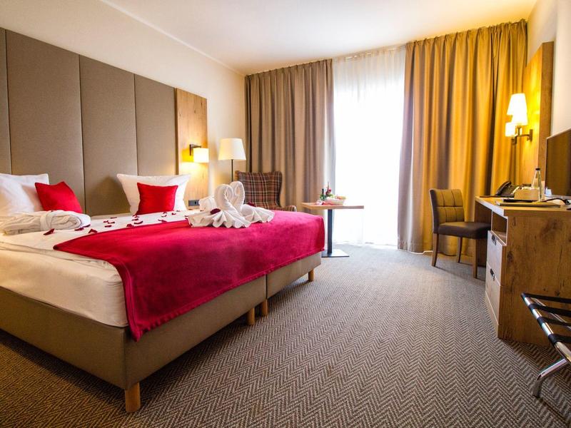 Modern eingerichtetes Hotelzimmer mit Doppelbett, Hellbraunem Teppich und großen Fenstern mit Vorhängen.