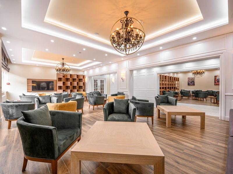 Großer, eleganter Raum mit modernen Sesseln, Holztischen, Kronleuchter und Spiegelwand.