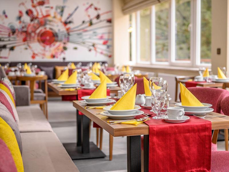 Restaurant mit gedeckten Holztischen, bunten Kissen, gelben Servietten und großem Fenster.