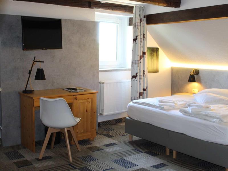 Moderní hotelový pokoj s postelí, stolem, židlí a televizí, dobře osvětlený.