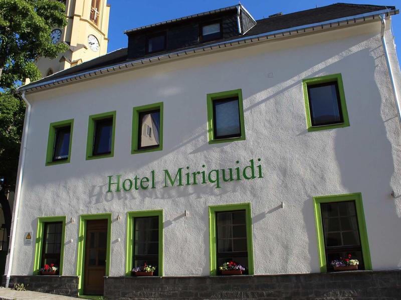 Bílá fasáda hotelu Miriquidi se zelenými rámy oken na slunci