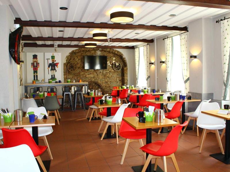 Moderní restaurace s červenými židlemi, dřevěnými stoly a dekorativním kamenným obloukem v pozadí.