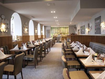 Ein heller, moderner Speisesaal mit Holzmöbeln, gedeckten Tischen und großen Fenstern.