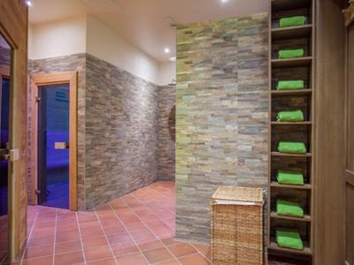 Moderner Wellnessbereich mit Steinwand, Fliesenboden, Holzmöbeln und grün gefalteten Handtüchern.