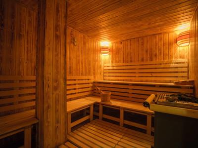 Holzsauna mit Bänken, warmem Licht und Saunaofen in einer Ecke.
