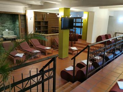 Innenraum eines Wartebereichs mit Holzmöbeln, Sesseln, gelben Säulen und Fliesenboden.